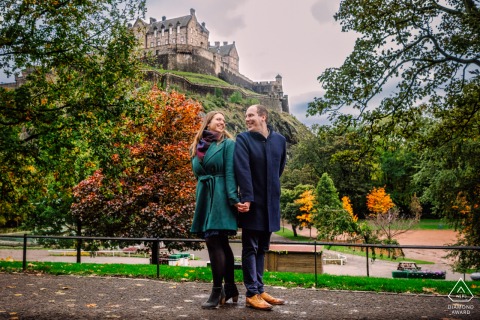 In Edinburgh, Scotland, a beautiful couple stands back to back, holding hands in front of the iconic Edinburgh Castle. This enchanting scene is expertly captured by a WPJA pro photographer.