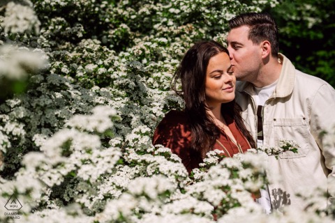 In a beautiful spring pre-wedding shoot at Rockanje Beach, the Netherlands, a couple is surrounded by a sea of blooming white flowers, skillfully captured by a WPJA pro photographer.