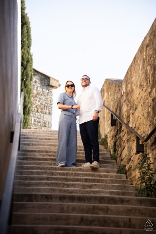 Couple stands on stone stairs in Grignan village, Drôme Provençale, viewed from low angle.