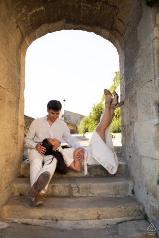 Couple shares a romantic cuddle in narrow cobblestone alleyways of picturesque Grignan, Drôme provençale.