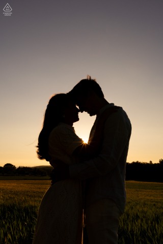 Silhouetted couple embraces romantically at sunset in Grignan, Drôme provençale, golden sky behind them.