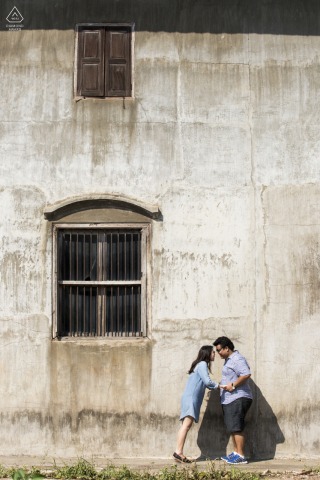Couple stands at stone building in Chantaburi, Thailand, sunlight casting dramatic shadows around them.