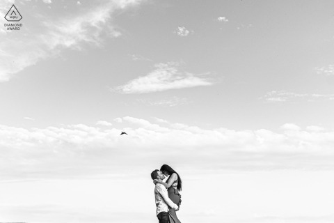 Minimalist portrait in Beauvoir de Marc, France: groom to be lifts bride to be, lovers under sky, pigeon flying.