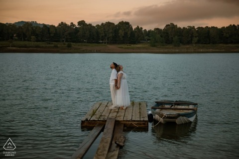 Couple stands back to back on Lago Piana degli Albanesi pier, peaceful, serene portrait by water.