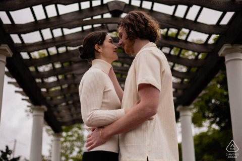 Tender Gaze Beneath Canopy: Couple’s Love Woven Between Brewster Gardens Columns, Plymouth Couple shares tender gaze beneath structured canopy at Brewster Gardens, Plymouth; love woven between columns.