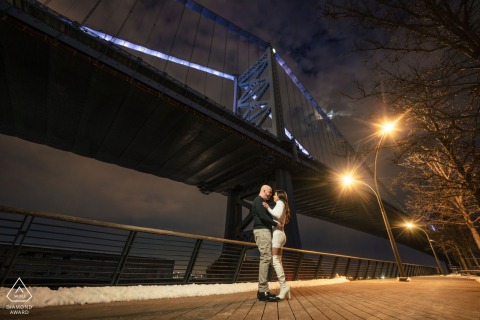 The couple embrace at Race Street Pier beneath Philadelphia’s iconic bridge.