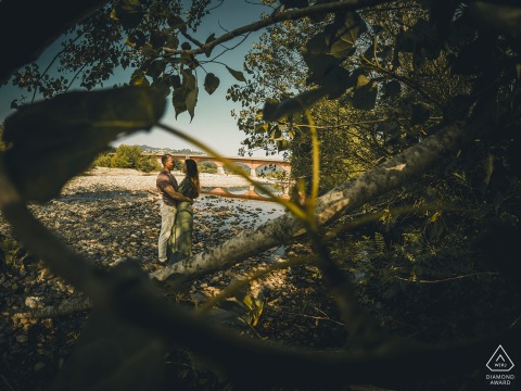 Engaged couple in Bolano, standing close together, photographed through trees.