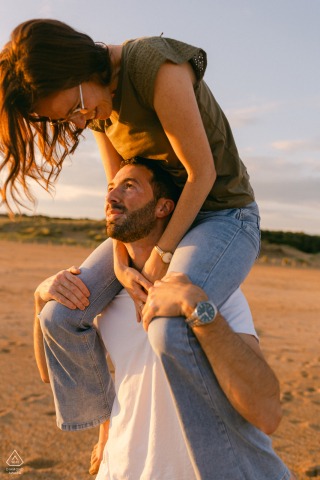 Engaged couple stands on Les Sables d'Olonne beach, backlit by warm, glowing sunset light.
