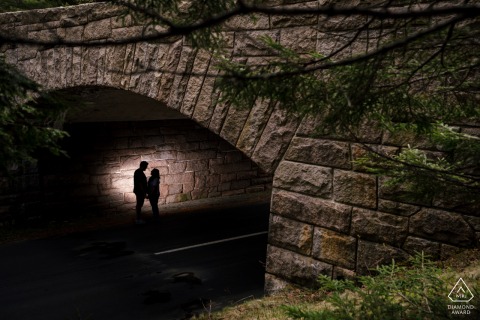 Affectionate Couple Poses Under Acadia’s Iconic Stone Bridge Amidst Lush Green Foliage Couple poses affectionately under Acadia National Park’s iconic stone bridge, surrounded by lush green foliage.