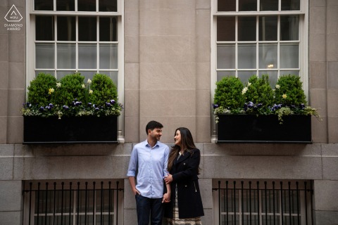 A couple stands together between flower-filled window boxes on a picturesque Beacon Hill, Boston street.