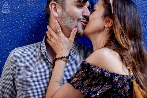 A couple shares an intimate kiss while standing against a striking blue wall in Paris, France.