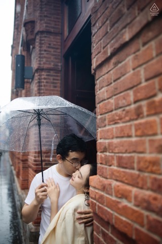 Engaged Couple Shares Tender Kiss by Red-Brick Building on Rainy Shanghai Bund Day Engaged couple shares a tender kiss by a red-brick building on rainy Shanghai Bund day.