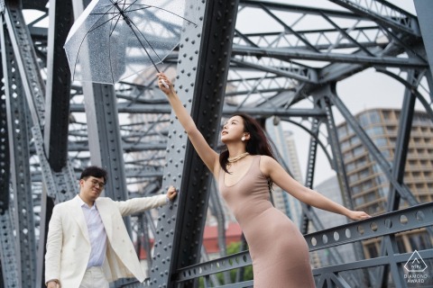 Engaged couple stands romantically on steel bridge, rainy day at the Bund, Shanghai, China.