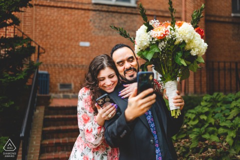 Engaged couple video chats with family, smiling, in charming downtown Annapolis, Maryland, during engagement photos.