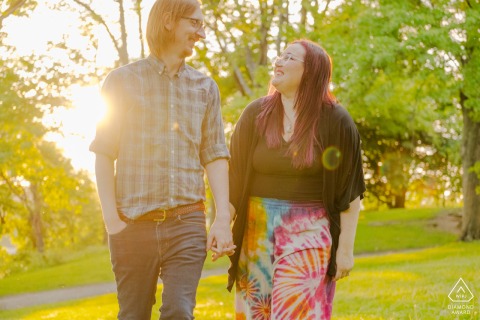 The engaged couple walk hand-in-hand in Highland Park, Pittsburgh, with the setting sun behind them.