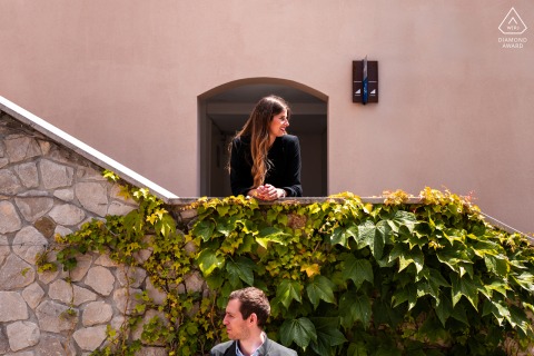 Alternative portrait in Portopiccolo: bride-to-be stands above groom-to-be on stairway, layered composition.