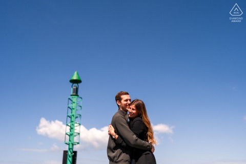 Engaged couple posing under blue skies, tower visible beside them in Portopiccolo, Sistiana, Trieste, Italy.