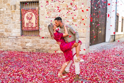 Pre-wedding couple kisses in Baeza, surrounded by falling red and white petals covering the ground.
