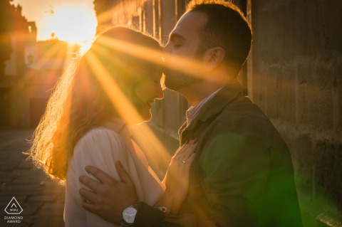 Engaged couple poses in afternoon light, sun rays crossing before them, Baeza, Jaén, Spain setting.