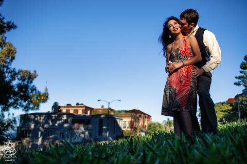 Engagement portrait of a San Francisco couple in a field with a distant building.