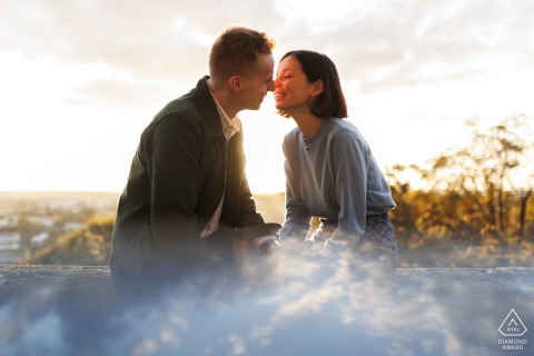 Engaged couple kisses on an old city wall in Angoulême, France at sunset.