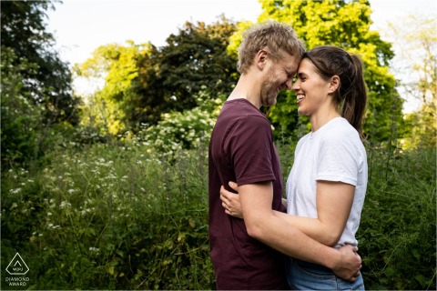 Summer engagement shoot at Verulamium Park, St Albans. A couple laughs in front of greenery.