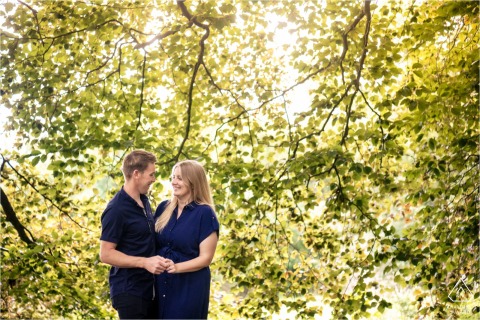 Verulamium Park, St Albans. Cuddling couple smiles under a canopy of summery trees.