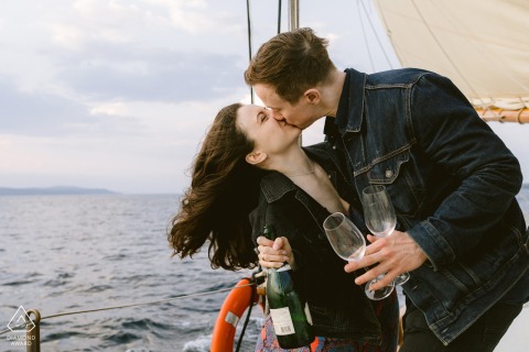 CAMDEN, Maine — A happy couple celebrates their engagement on a schooner, holding a celebratory toast with a bottle and glasses while sailing on the scenic Maine coast.