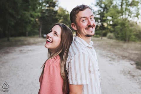 GIRONDE, France — A couple shares a laugh during their engagement portrait session at Lac Vert de Canéjan. Positioned back-to-back, they showcase their playful connection and joy.