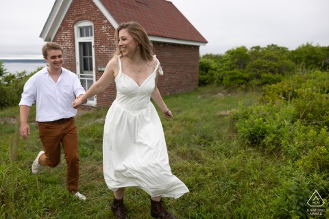 GEORGETOWN, Maine — A joyful couple runs hand-in-hand across a grassy field near a red brick building. This engagement portrait captures their playful connection on Seguin Island.