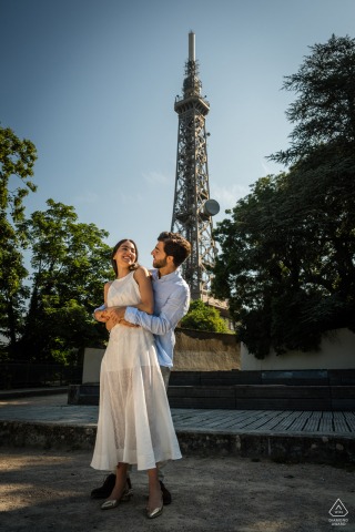 PARIS — A smiling couple embraces against a backdrop reminiscent of the Eiffel Tower. The playful pair enjoys a lighthearted engagement portrait, their affection a beautiful secret in the city of love.
