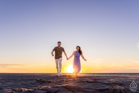 DENNIS, Mass. — A couple races hand-in-hand along Mayflower Beach, against the low sun. This engagement portrait captures their youthful, carefree love.