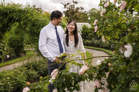 Boston's Kelleher Rose Garden Engagement: A Romantic Portrait of a Laughing Couple BOSTON — Surrounded by blooming roses at the Kelleher Rose Garden, a cheerful couple shares a laugh during their engagement session, their joy shining through this romantic portrait.