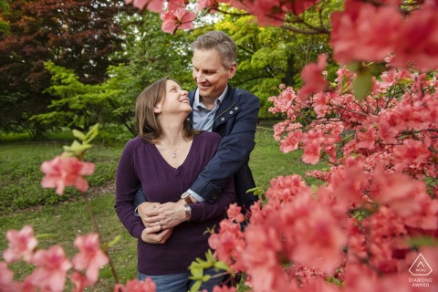 BOSTON — Surrounded by vibrant pink and red blooms, a couple embraces at the Arnold Arboretum. This engagement portrait captures their affection within the colorful floral landscape.