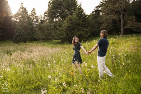 BOSTON, MA - A Couple's Love Story Unfolds at the Arnold Arboretum BOSTON — A woman leads her partner through a field of tall grass, their hands clasped. This engagement portrait captures the couple's genuine connection amidst the natural beauty of the Arnold Arboretum.