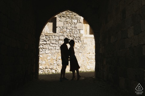 LECTOURE, France — A couple shares a romantic kiss, silhouetted in an ancient archway at The Castelnau. This intimate engagement portrait captures their passion and timeless connection.