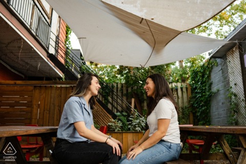 MONTREAL, Quebec — An engaged couple shares a warm and intimate gaze while seated at a picnic table under a shady canopy, a tender scene captured during their portrait session.
