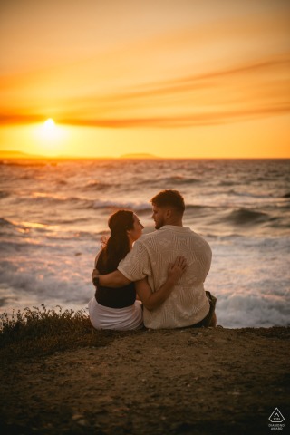NAXOS, Greece — A couple sits close together, watching the sun descend over the Aegean Sea. This serene portrait captures their deep connection against a stunning sunset backdrop.
