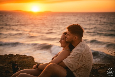 NAXOS, Greece — A couple watches the sunset together from a rocky shore. This intimate portrait captures their shared affection with the sun setting over the Aegean Sea.