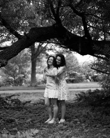 BOSTON — A couple shares a laugh in a black-and-white portrait, standing together beneath a tree's branches. The engagement session captures their happiness at Christian Herter Park.