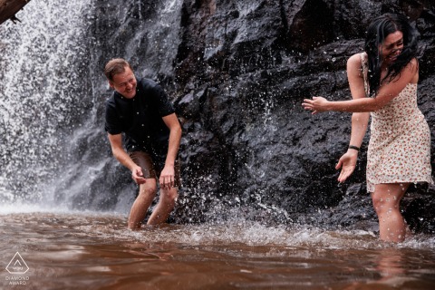 Splashing Into Forever: Duluth, MN Waterfall Engagement Amidst Rocks and Cascading Water An engaged couple playfully splashes in a Duluth, MN waterfall, surrounded by rocks and cascading water.