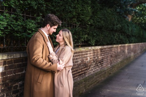 Gazing Lovingly: An Engagement Portrait Beside a Brick Wall in the City of London Engaged couple gazes into each other's eyes, standing beside a short brick wall in City of London, outdoor portrait.