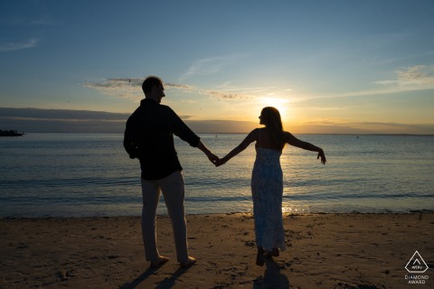 Recently engaged couple in Falmouth, Massachusetts stands joyfully into a vibrant sunset, silhouetted.