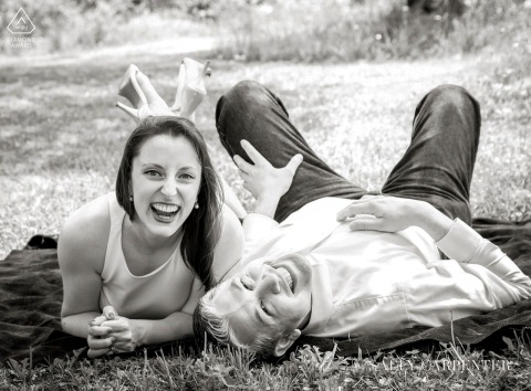 Laughing With You on a Picnic Blanket in Vermont's Green Grass Engaged couple lies on a picnic blanket in green grass at Featherstone, Woodstock, Vermont, laughing joyfully during photo session.