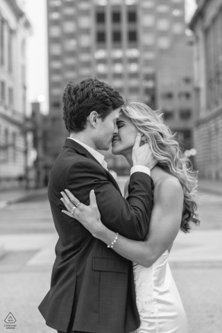 Engaged couple in downtown Cleveland, Ohio: sharing a romantic embrace and kiss, city buildings softly blurred in the background.