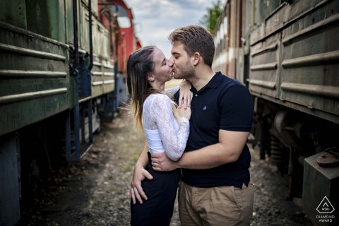 Budapest, Hungary — A couple shares a kiss between vintage trains, uniting historic charm and new adventures in this evocative and romantic portrait.