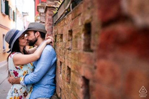 Italian Alley Kiss: Timeless Urban Romance in a Caorle Engagement PortraitItalian Alley Kiss: Timeless Urban Romance in a Caorle Engagement Portrait Caorle, Venice, Italy — A couple kisses in a red brick alley, capturing urban romance and timeless charm in this intimate portrait.