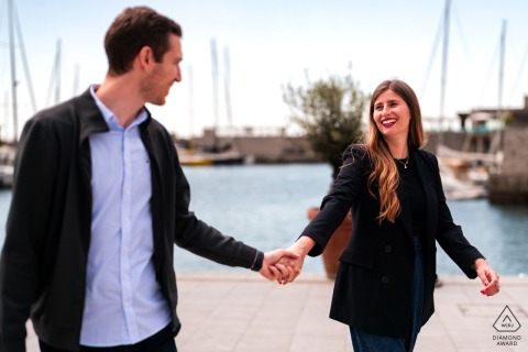 Portopiccolo, Sistiana, Trieste, Italy — A couple walks hand in hand, laughing together in the sun by the water, capturing a joyful and relaxed portrait.