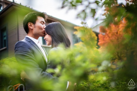 UC Berkeley — A couple is framed by lush foreground foliage as he kisses her forehead, capturing a tender and romantic engagement portrait on campus.
