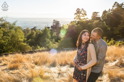 Oakland, California — A couple stands atop a sunlit knoll surrounded by dry grasses, highlighting their connection in this warm and natural Northern California engagement portrait.